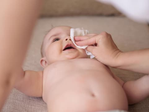 Mutter wischt ein verklebtes Auge beim Baby sauber.