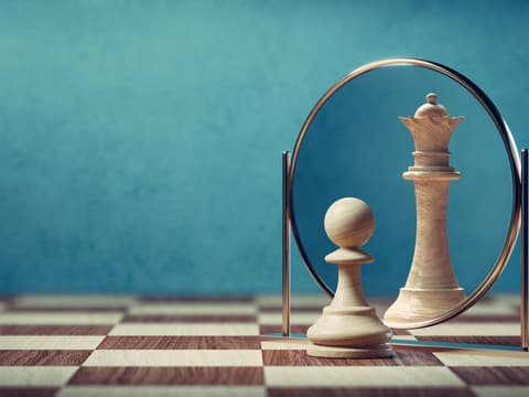 Darstellung einer Bauernfigur beim Schach, die im Spiegel eine Dame sieht