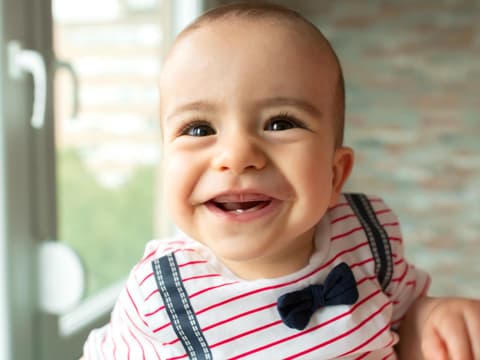 Baby mit frischem Zahn lacht in die Kamera.