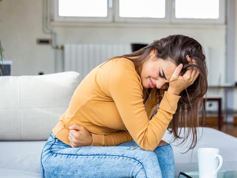 Frau sitzt auf Sofa und starke Bauchschmerzen