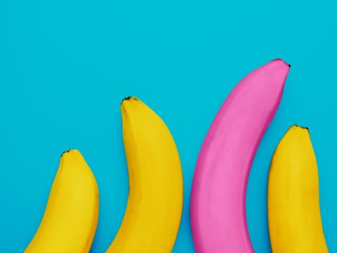 Eine lange pinke Banane neben drei kleineren gelben Bananen als Symbol für unterschiedliche Penislängen
