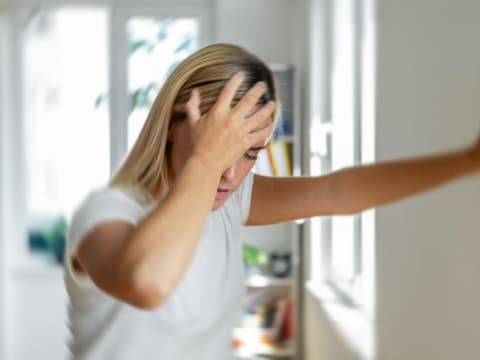 Frau hat Schwindel und muss sich an einer Wand abstützen