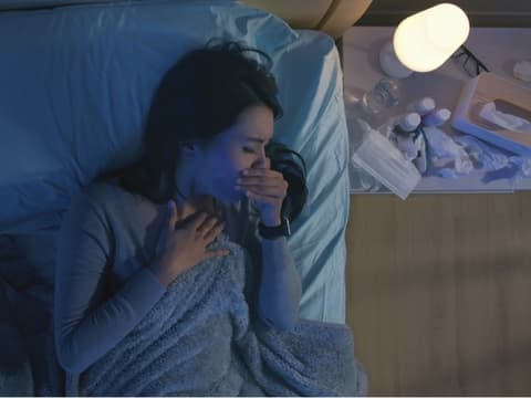 Frau liegt auf dem Bett und hustet