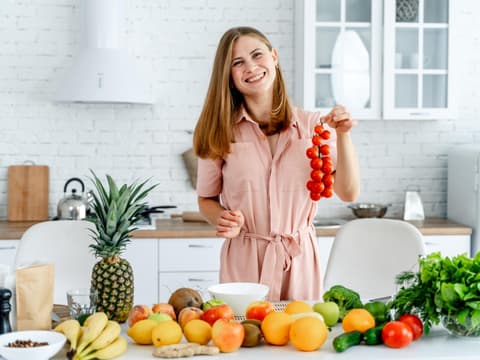 Frau steht in der Küche und bereitet eine Mahlzeit mit Gemüse und Obst zu.