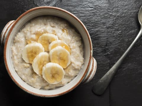 Draufsicht einer Schüssel Porridge mit Bananenscheiben und Honig
