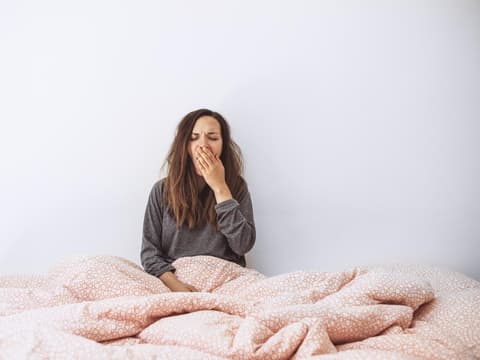 Frau sitzt im Bett und gähnt