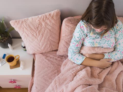 Junge Frau liegt im Bett hält sich den Bauch 
