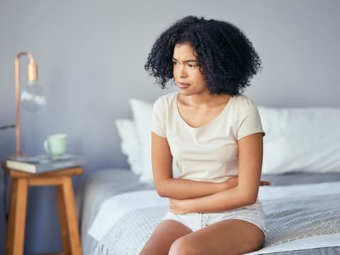 Frau mit Unterleibschmerzen sitzt im Bett