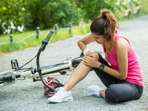 Junge Frau hatte einen Unfall mit dem Fahrrad und hält sich das Knie.