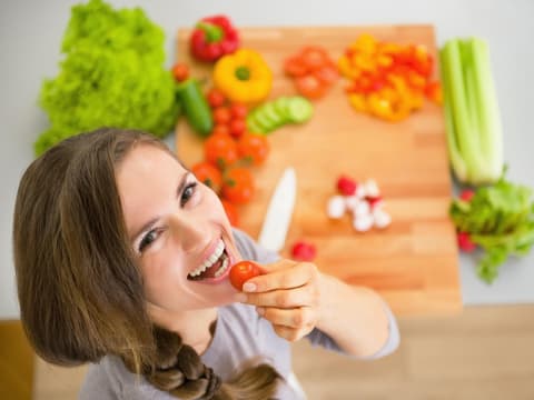Frau steht vor einem Brett mit Gemüse und isst eine Tomate