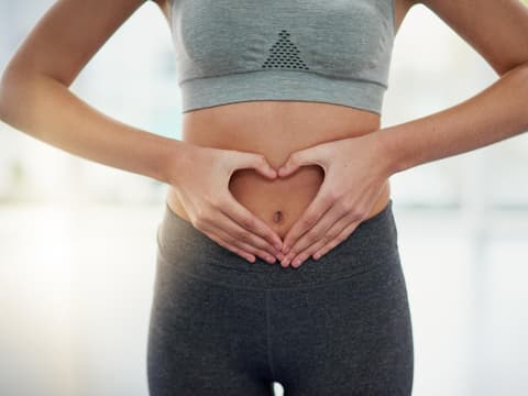 Frau im Sportoutfit zeigt mit ihren Händen ein Herz auf Bauchhöhe