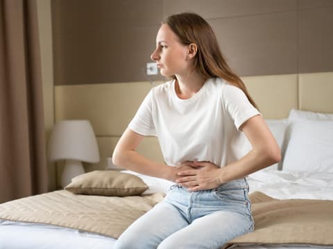 Frau sitzt auf dem Hotelzimmerbett und hält sich den Bauch