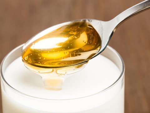 Honig wird in eine Tasse voller Milch geschüttet