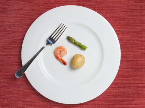 Großer Teller mit einer kleinen Kartoffel, einem Shrimp und einem Stück grünem Spargel darauf