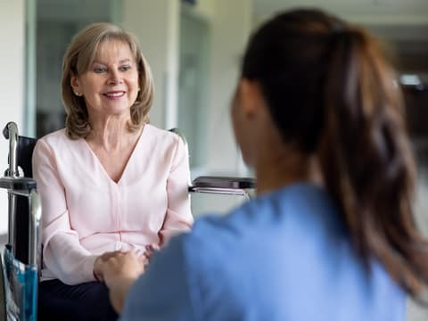 Frau sitzt im Rollstuhl und wird von Krankenschwester betreut