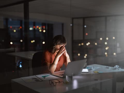 Überarbeitete Frau sitzt spät am Abend im leeren Büro 