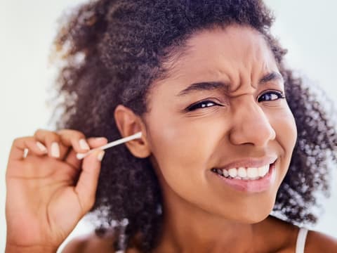 Frau reinigt ihre Ohren mit Wattestäbchen und verzieht das Gesicht