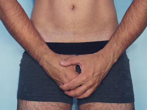 Mann hält sich die Hände schützend vor den Intimbereich