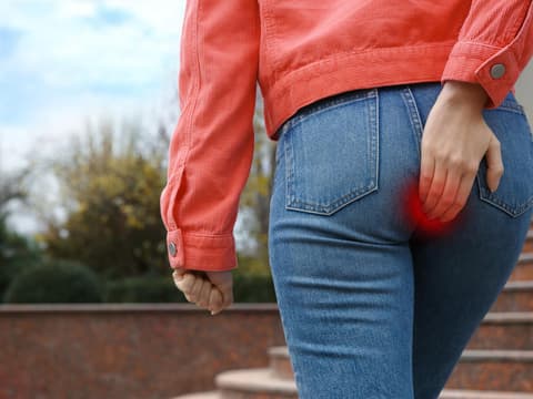 Frau fasst sich an den Po, wo sie Schmerzen hat