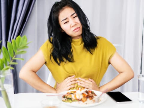 Frau hält sich den Bauch beim Essen