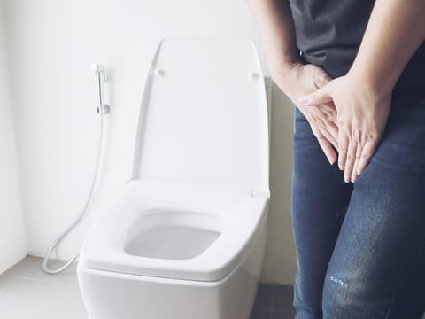 Person hält sich vor Toilette die Hände vorm Schritt