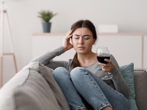 Frau sitzt mit einem Glas Wein in der Hand auf dem Sofa und fühlt sich unwohl