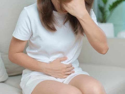 Gestresste Frau sitzt auf dem Sofa und hält sich den Bauch