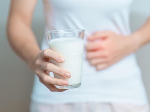 Frau hält ein Glas Milch in der einen Hand und fasst sich mit der anderen an den Bauch