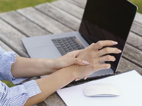 Frau sitzt vor Computer und hält schmerzende Hand