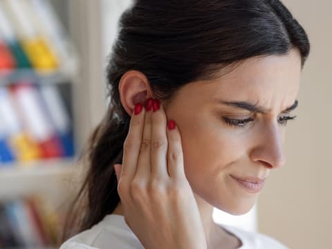 Frau hält sich mit besorgter Miene eine Hand ans Ohr