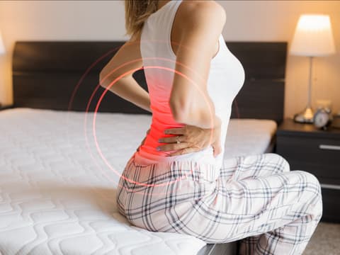 Frau sitzt auf dem Bett und hat Rückenschmerzen