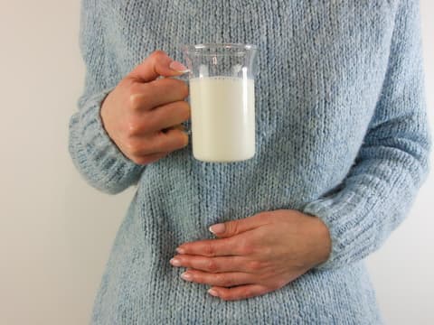 Frau mit Glas Milch in der Hand hält sich den Bauch