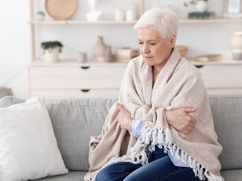 Frau sitzt mit einer Decke um die Schultern auf dem Sofa