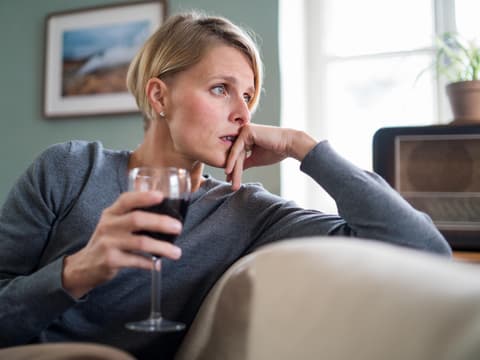 Nachdenkliche Frau sitzt auf dem Sofa mit einem Glas Wein in der Hand
