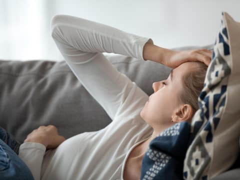 Frau liegt auf dem Sofa und fühlt sich schlecht