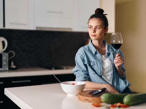 Frau steht in der Küche und trinkt Wein