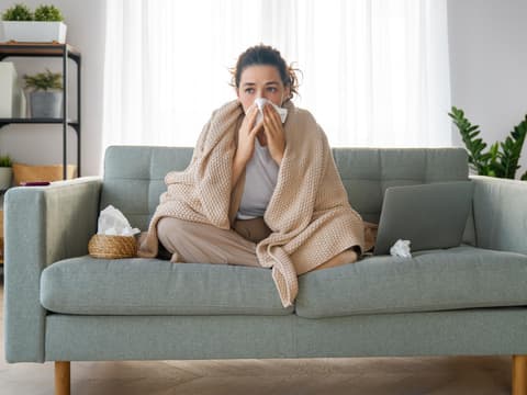 Erkältete Frau sitzt auf Sofa
