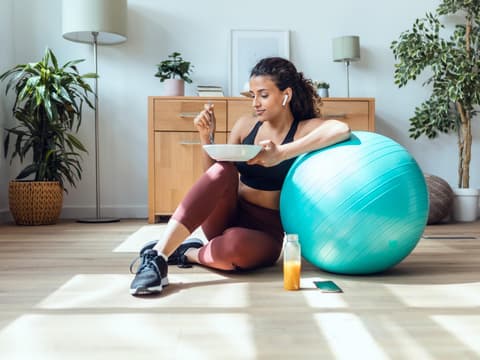 Frau sitzt neben Gymnastikball mit gesundem Essen