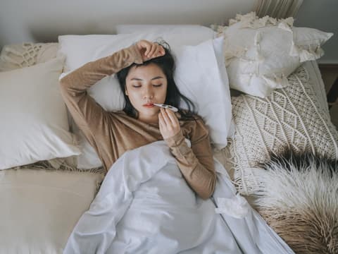 Frau liegt mit Fieberthermometer im Bett