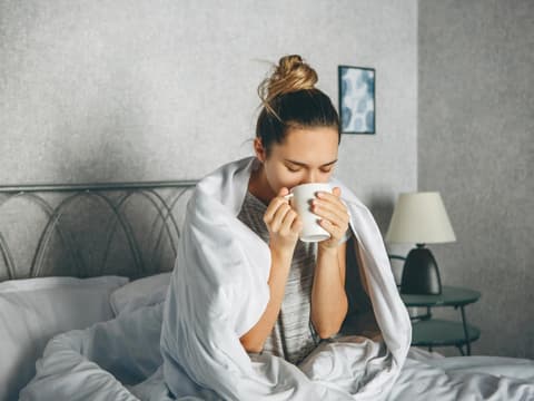 Frau sitzt im Bett und trinkt Tee