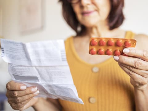 Frau liest Beipackzettel von Medikamenten