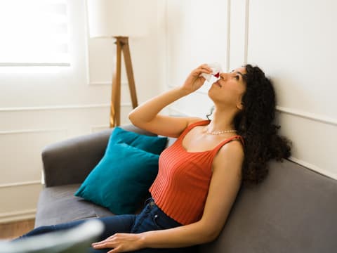 Frau sitzt auf einem Sofa und hat Nasenbluten
