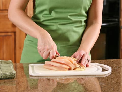 Frau schneidet rohes Hähnchen auf einem Schneidebrett