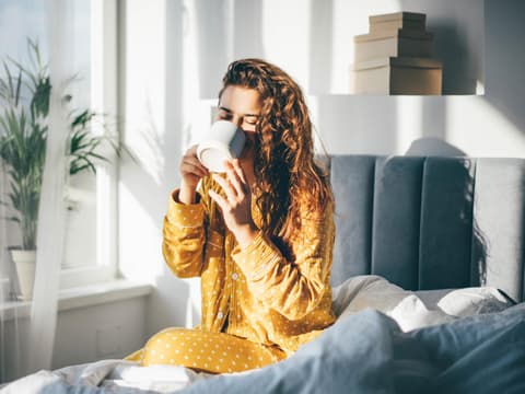 Frau trinkt im Bett eine Tasse Kaffee