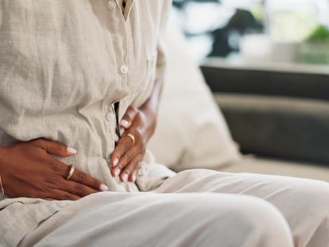 Frau sitzt auf dem Sofa und hält sich den Bauch.