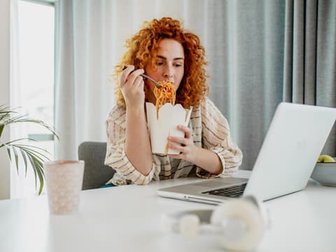 Frau isst Nudeln vor dem PC