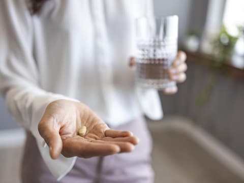 Frau hält eine Tablette in der einen und ein Glas Wasser in der anderen Hand
