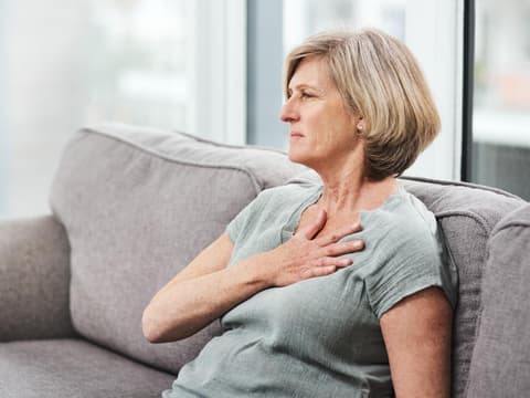 Frau sitzt auf dem Sofa und fasst sich an die Brust