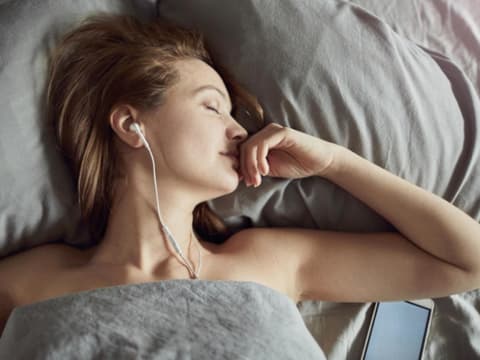 Frau liegt mit Kopfhörern im Bett