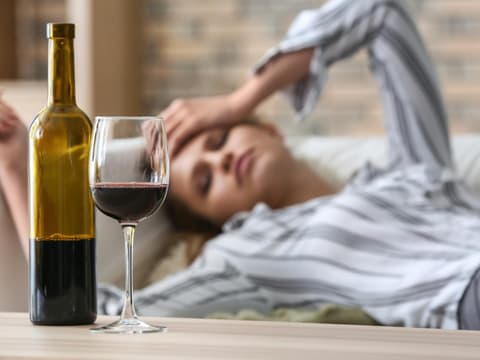 Offene Flasche Rotwein, Frau liegt auf einem Sofa